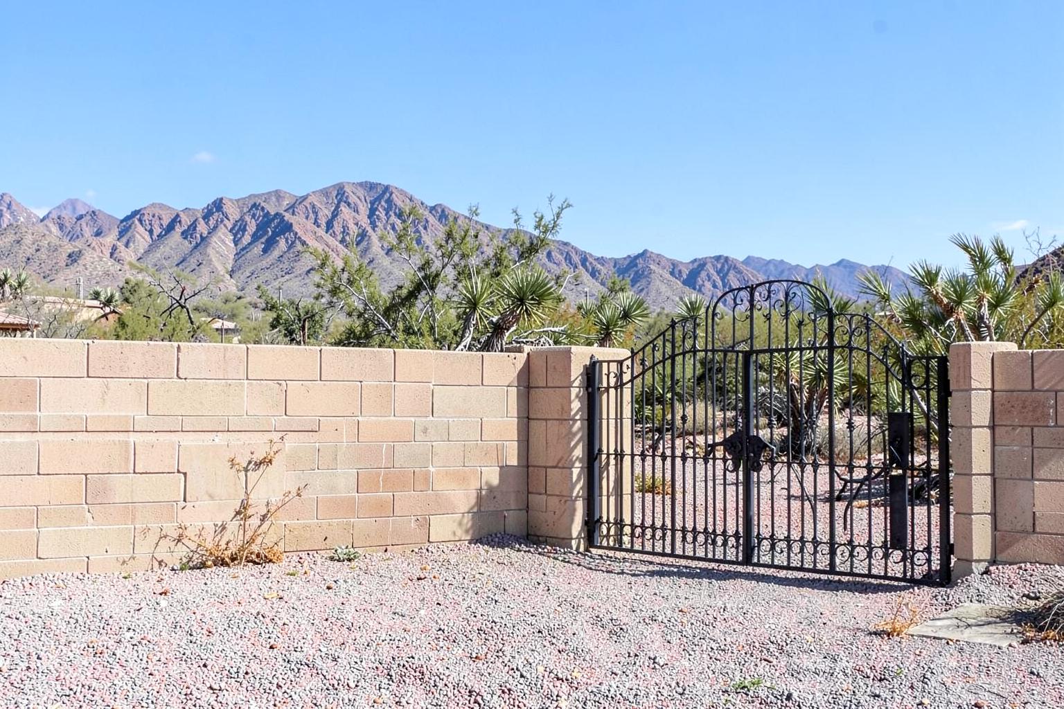 New block wall and wrought iron gate around a gravel desert property with mountains behind