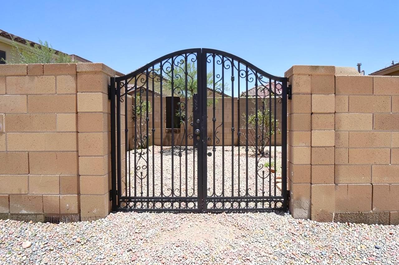 New wrought iron gate set into a tan block wall at a desert suburban home with gravel yard
