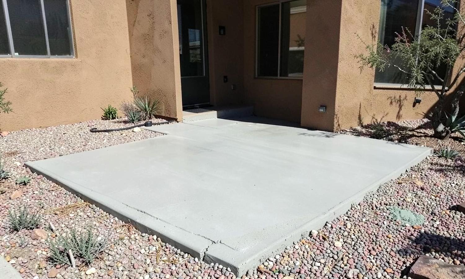 Freshly finished concrete patio slab beside a tan stucco desert home with gravel landscaping