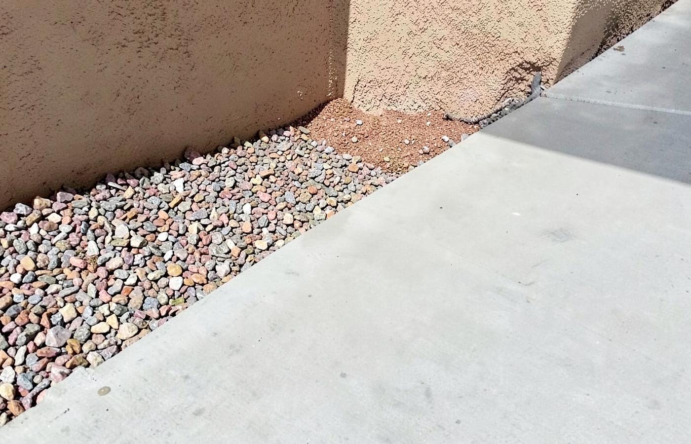 Close view of a smooth new concrete driveway edge meeting desert gravel beside a stucco wall in bright sun