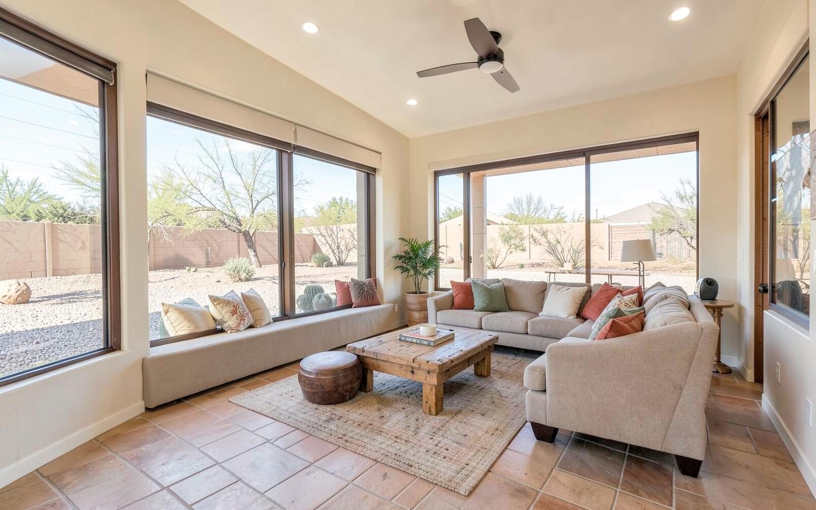 Bright southwestern living room with tile floors and large shaded windows looking onto a gravel desert yard