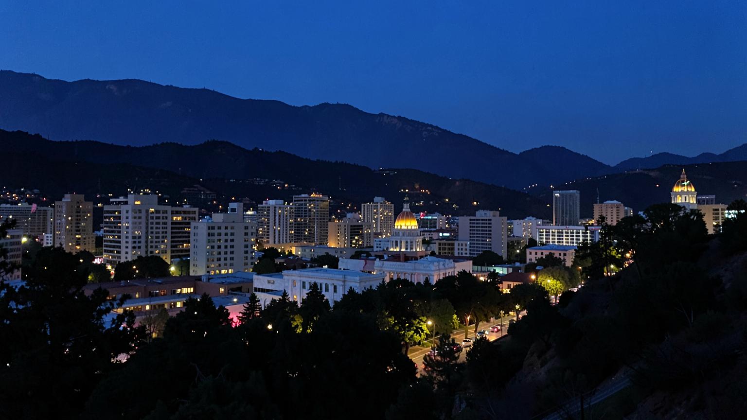 Downtown skyline at dusk with lit office buildings and dark foothills rising behind