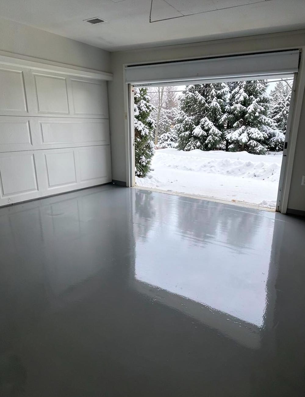 Glossy grey epoxy coated garage floor with the door open onto a snowy evergreen driveway