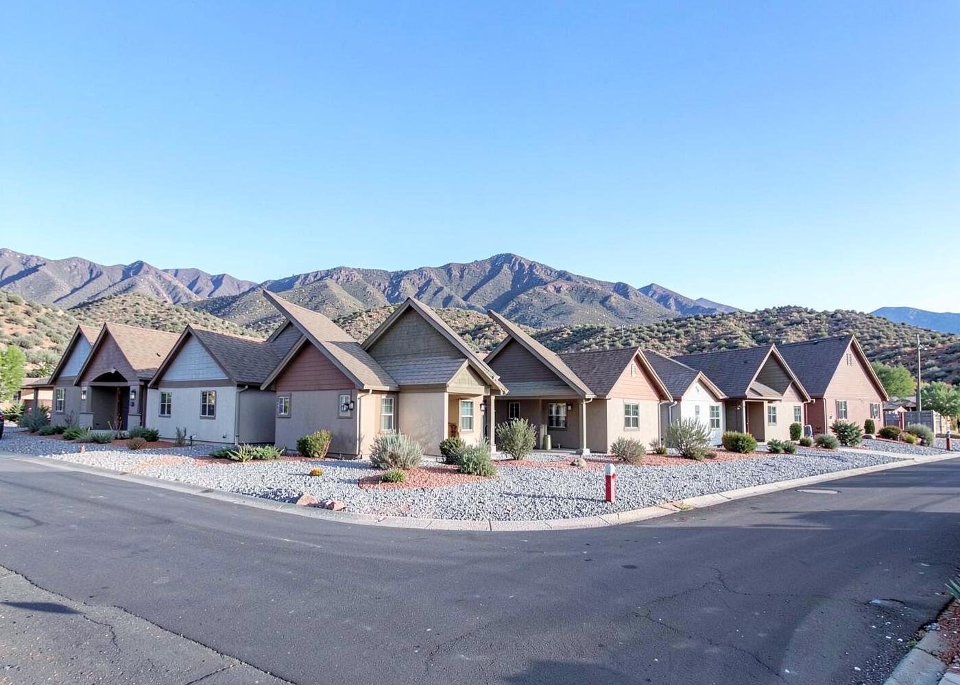 Row of modest single-story homes with pitched roofs and gravel front yards in a small high-desert subdivision below dry mountains