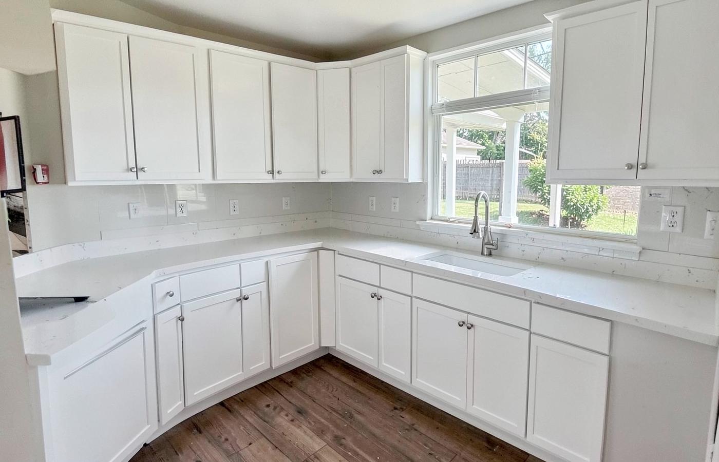 Newly renovated suburban kitchen with white cabinets and stone counters, unfurnished