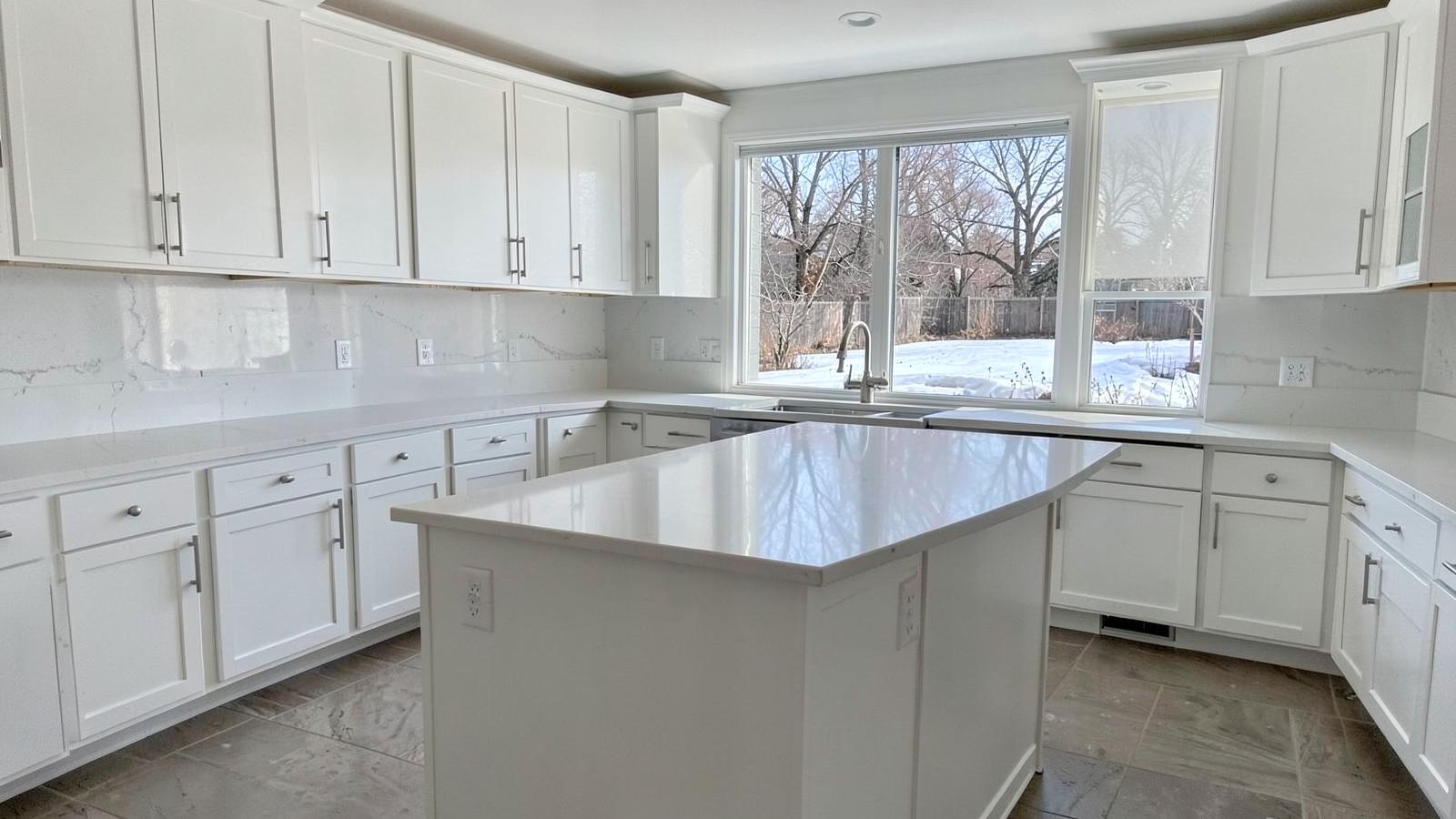 Bright white kitchen with quartz counters and a large window looking onto a snowy backyard