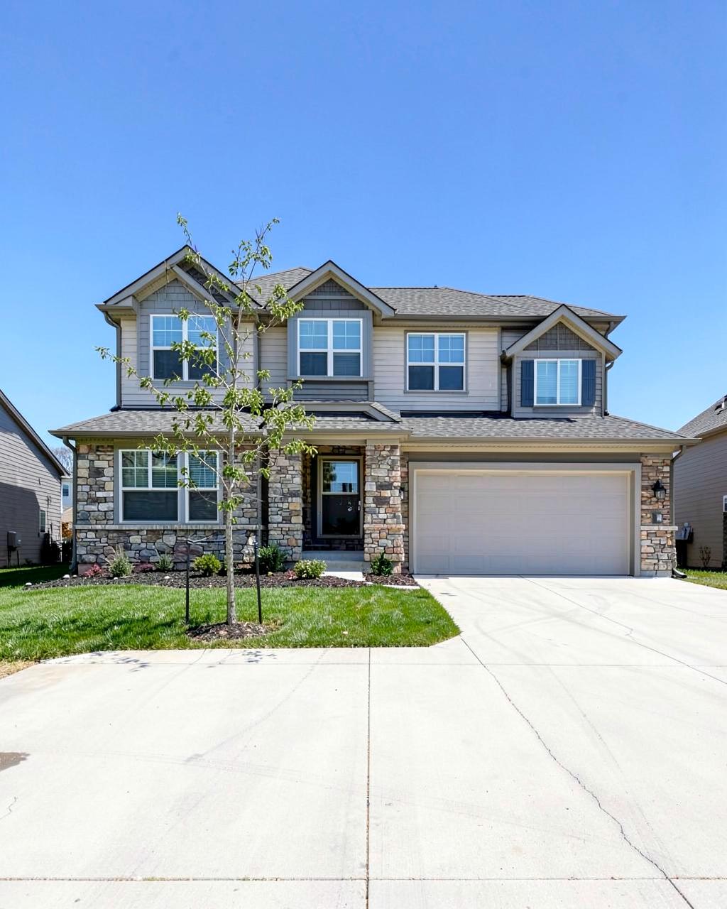 Front elevation of a newly completed two story suburban home with stone accents, new sod and a wide driveway