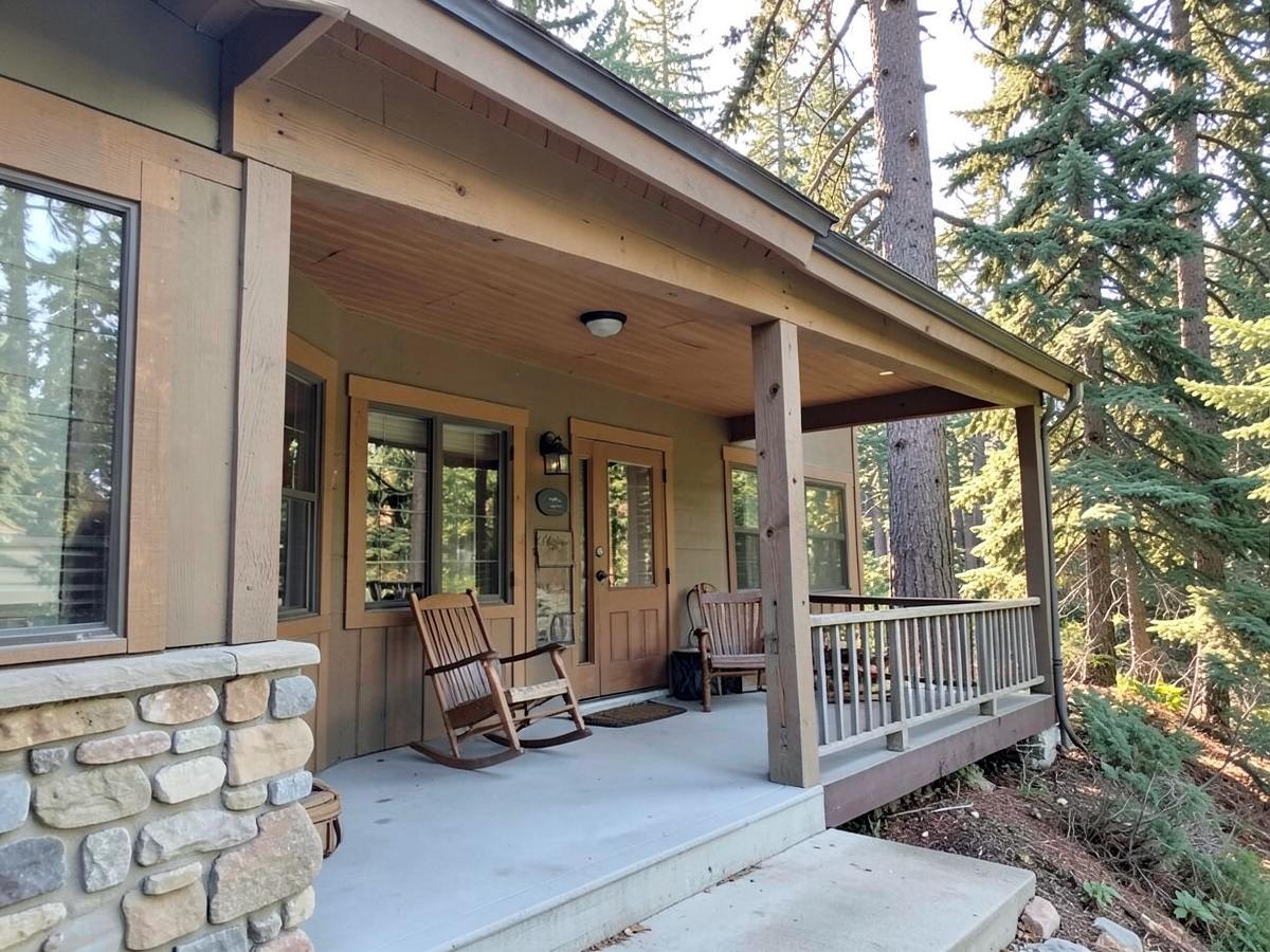 Covered craftsman front porch with a rocking chair surrounded by tall evergreen trees in morning light