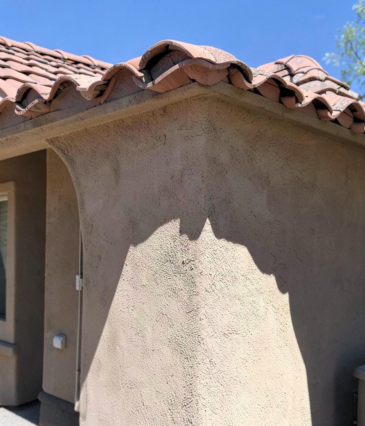Close view of a stucco wall corner and tile roof edge on an entry-level desert home in hard sunlight