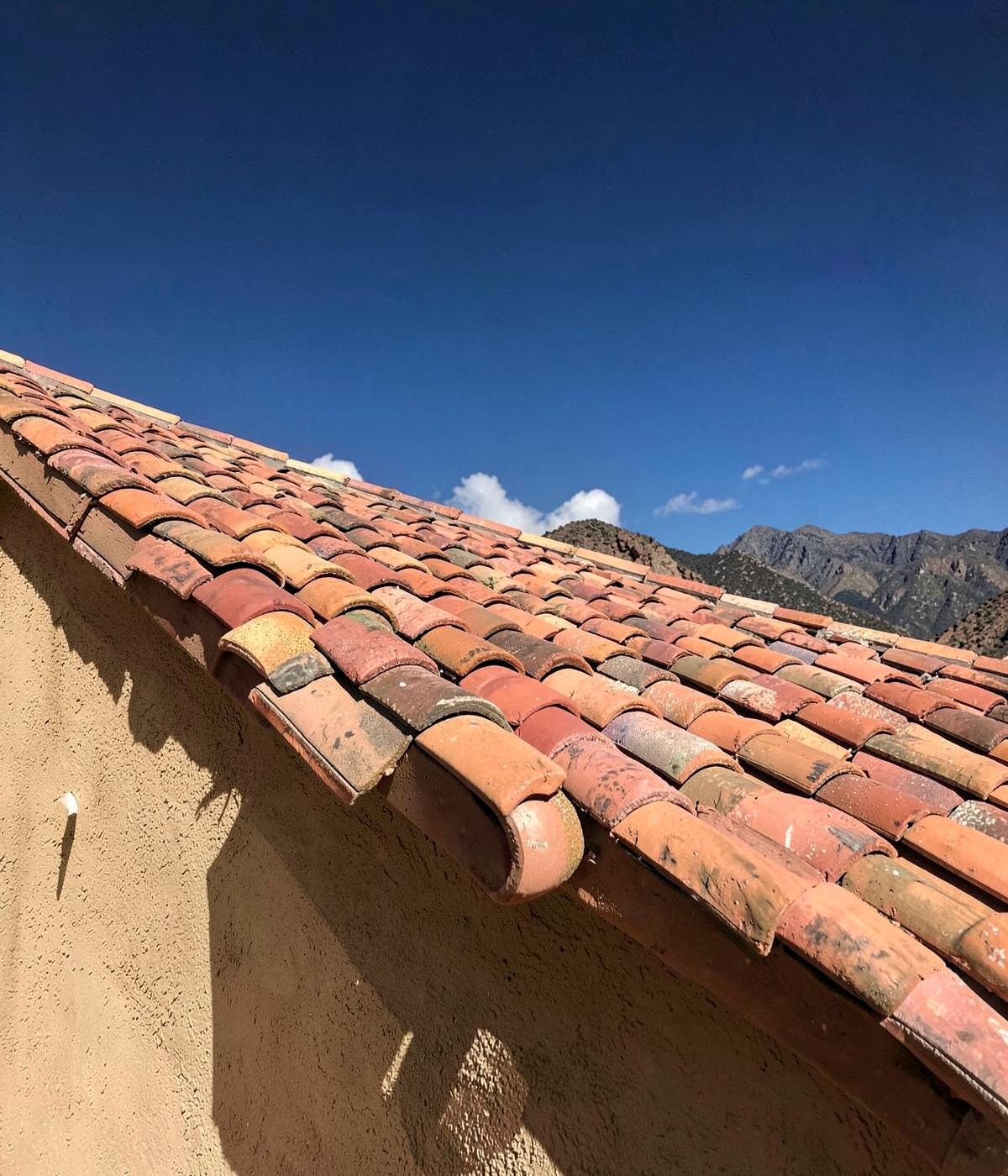 Sun-bleached clay barrel tile roofing on a stucco home against a deep blue sky with distant mountains