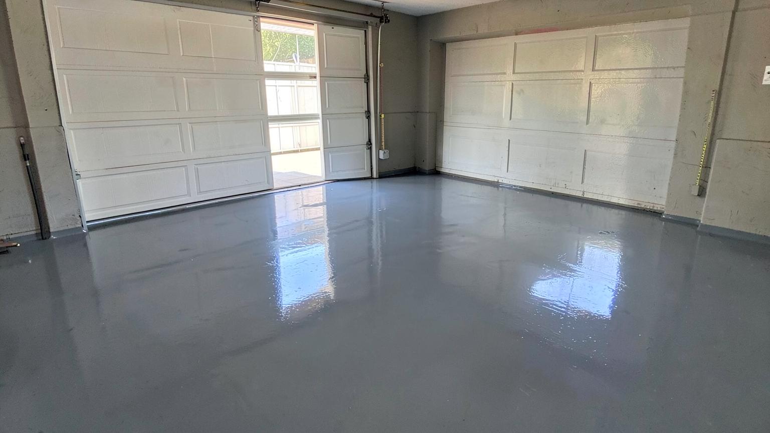 Freshly coated glossy grey epoxy floor in an empty two-car suburban garage with daylight through the open door