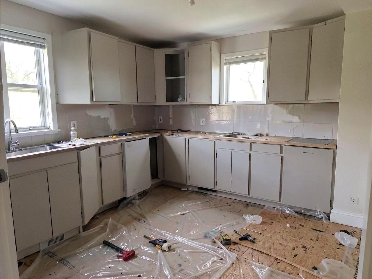 Kitchen mid-renovation with cabinets partly installed, plastic sheeting on the floor and tools on plywood