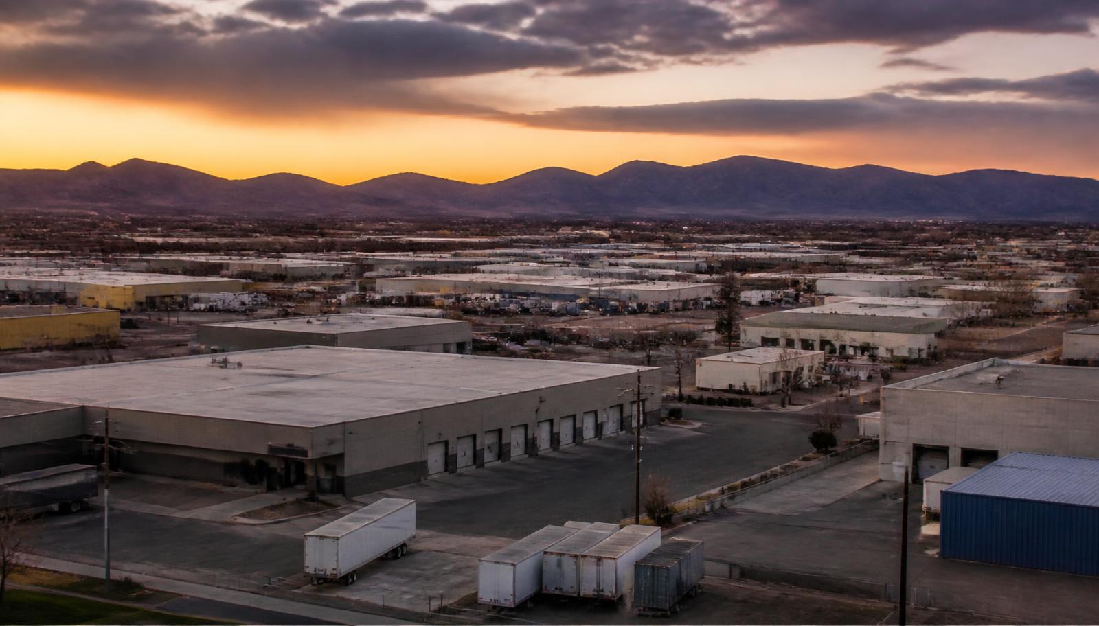 Low light-industrial warehouse blocks and loading bays on a flat valley street at the edge of a residential neighborhood